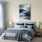 Coastal wave canvas hanging above a pale blue and white bed with striped blue and white linen and blue curtains in a coastal inspired room. Light wood bedside tables and a leight beige rug