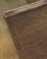A close-up of a brown textured area rug with a fringed edge, laid out on a light brown wooden floor.