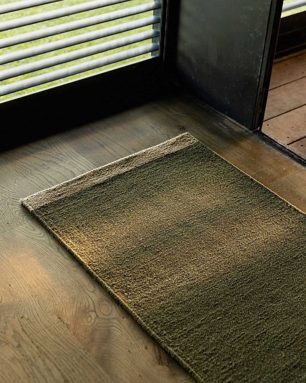 green entrance mat by louvered window and on wooden floor