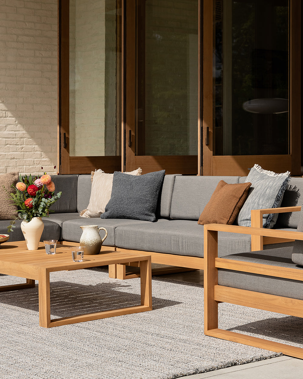 Outdoor patio furniture set with gray cushions and wooden frames on a patio.