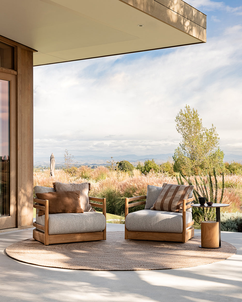 Two wooden chairs with cushions on a patio with a scenic view.