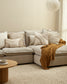 Beige sectional sofa with decorative pillows and a blanket in a living room setting.