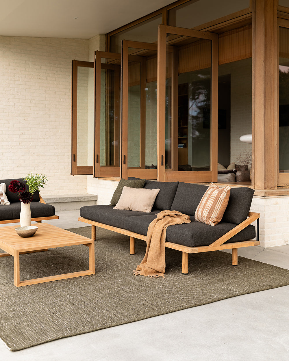Outdoor patio with gray sofa, wooden coffee table, and decorative elements.