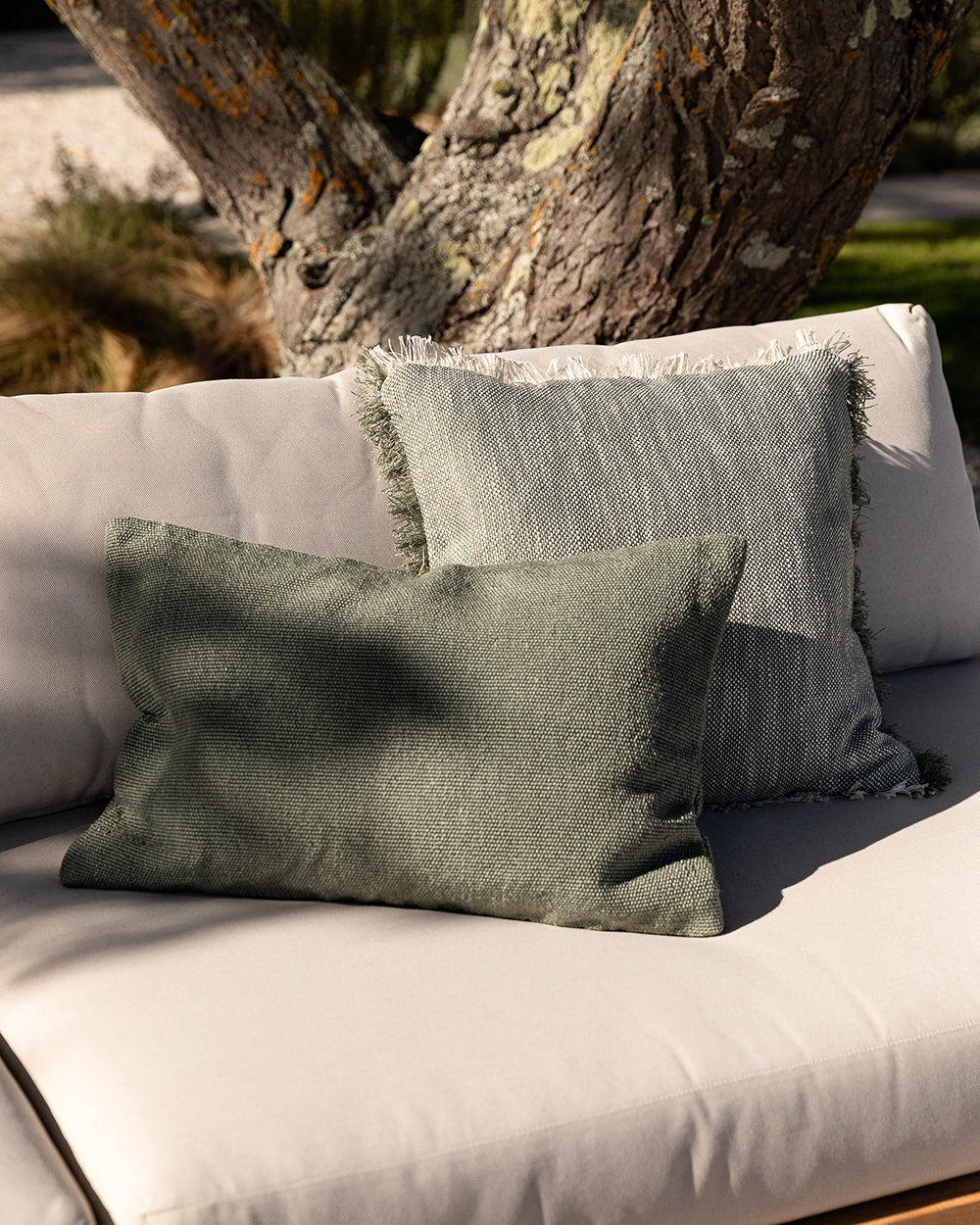 Green and gray cushions on a white outdoor sofa with a tree in the background