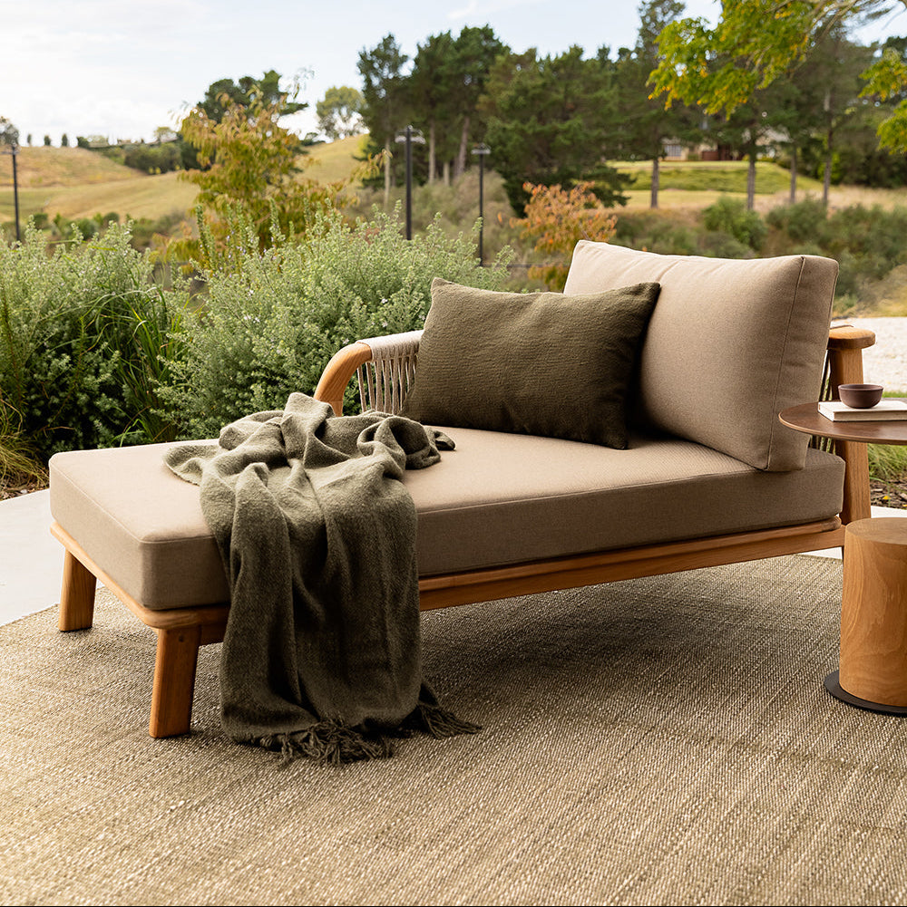 Outdoor sofa with cushions and a blanket in a garden setting