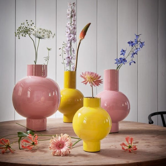 round metal vases, pink vases and yellow vases on a wooden table with strands of flowers in each vase