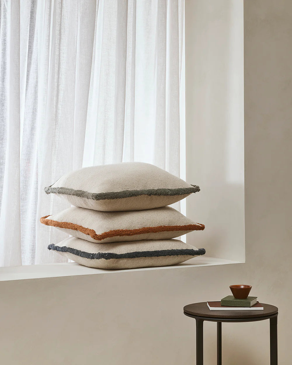 Stack of decorative pillows on a windowsill with a minimal background