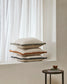 Stack of decorative pillows on a windowsill with a minimal background