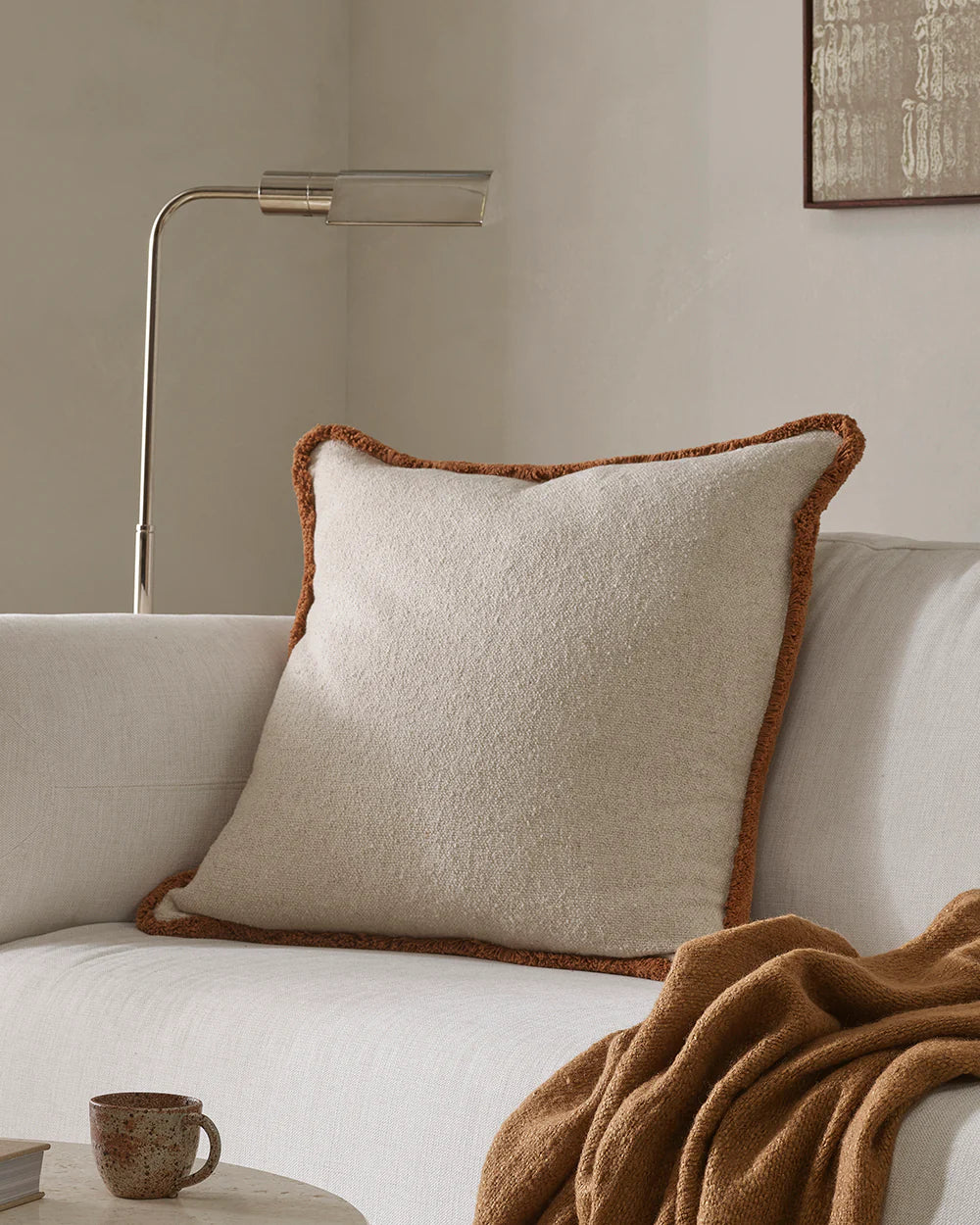 Beige pillow with brown trim on a white sofa in a cozy living room setting.