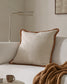 Beige pillow with brown trim on a white sofa in a cozy living room setting.