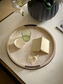 Round decorative tray with a glass, bowl, and book on a marble surface.