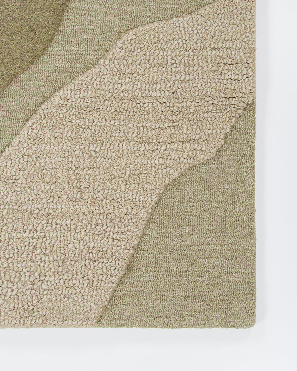 A close-up of a textured area rug with abstract organic shapes in beige and olive green, showing the looped pile texture and woven edges against a white background.