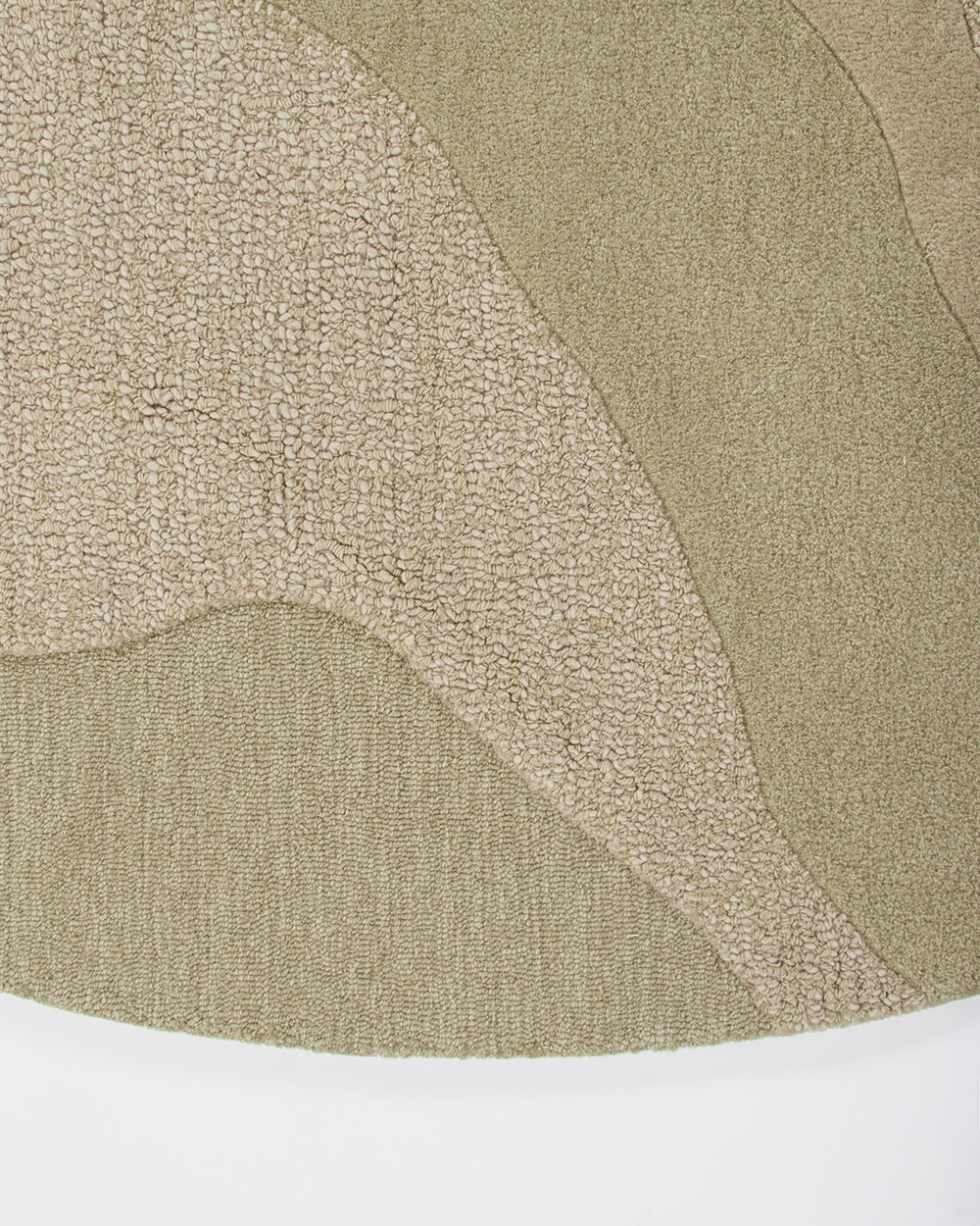 A close-up of a textured area rug with an abstract organic pattern in shades of beige and green, showing the pile texture and a white surface underneath.