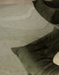 A close-up of a textured area rug with organic wavy lines in light sage green and cream, styled with dark olive green floor cushions.