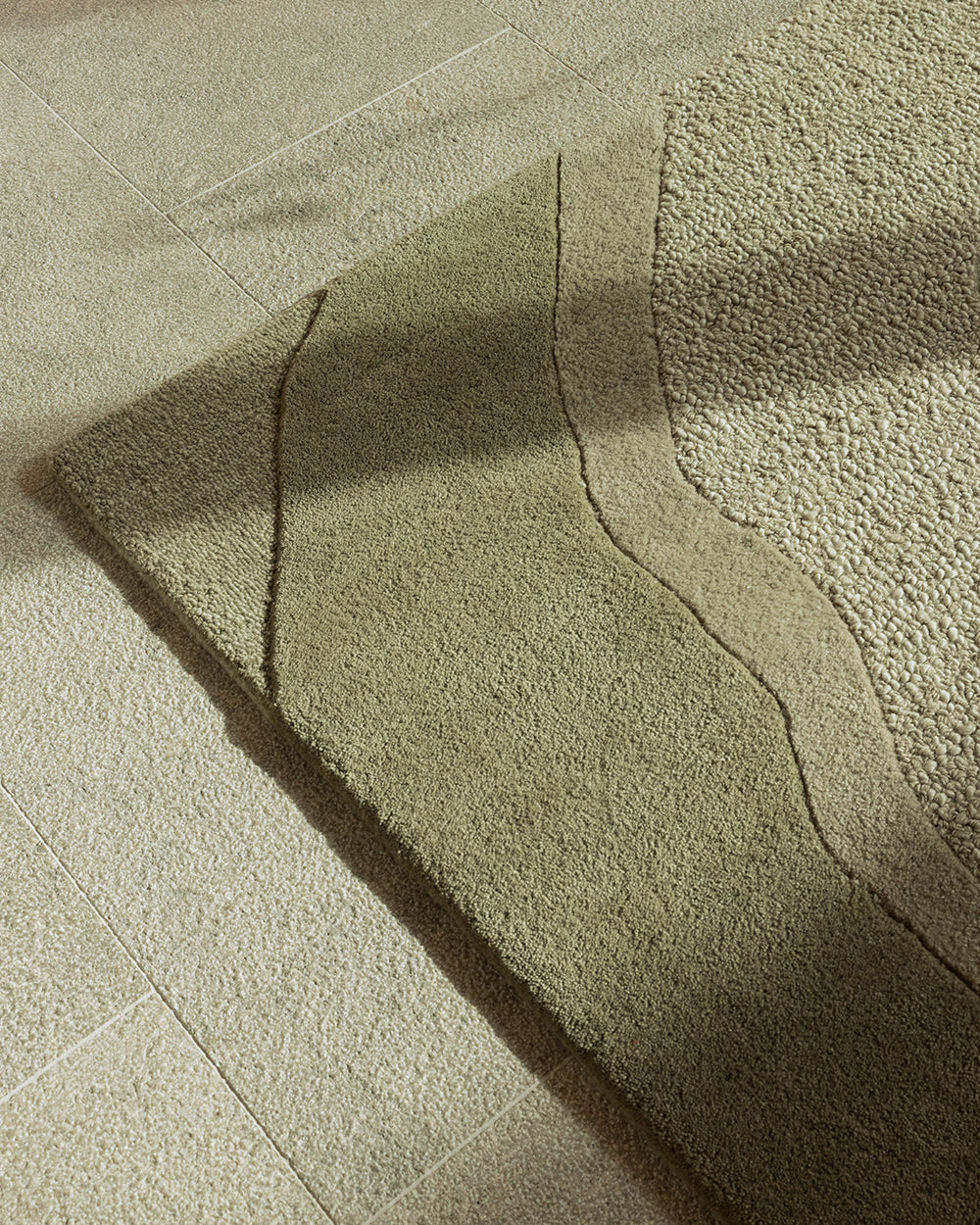 A close-up of a textured area rug with a wavy organic pattern, shown laid out on a light beige tiled floor with soft natural shadows.
