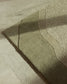 A close-up of a textured area rug with a wavy organic pattern, shown laid out on a light beige tiled floor with soft natural shadows.