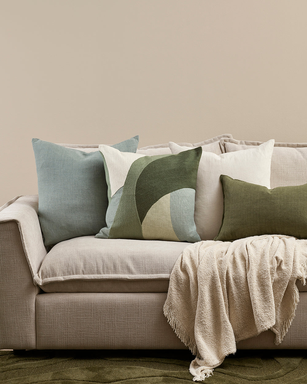 Gray sofa with Ellis decorative pillows and a blanket against a beige wall