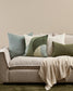 Gray sofa with Ellis decorative pillows and a blanket against a beige wall