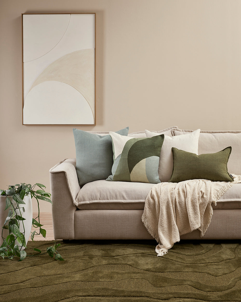 Beige sofa with decorative pillows and a blanket in a living room setting.