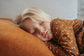Child sleeping on a soft surface wearing a brown outfit with white patterns.