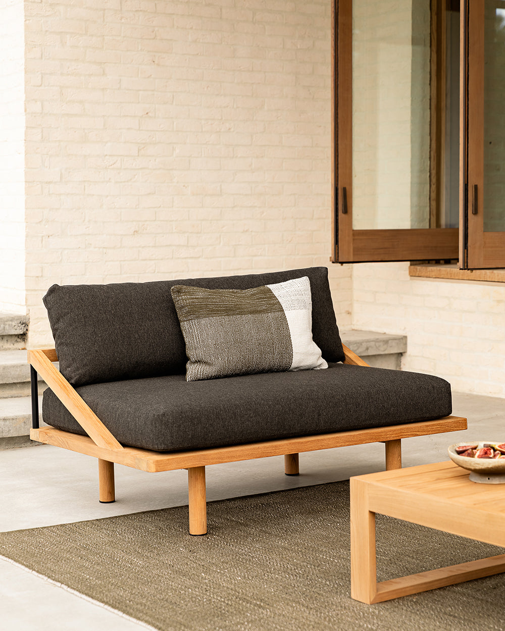 Outdoor sofa with cushions on a patio area with a neutral wall and wooden coffee table.