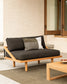 Outdoor sofa with cushions on a patio area with a neutral wall and wooden coffee table.