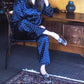 A woman wearing a navy blue pajama set with white polka dots sits on a chair in a home interior setting.