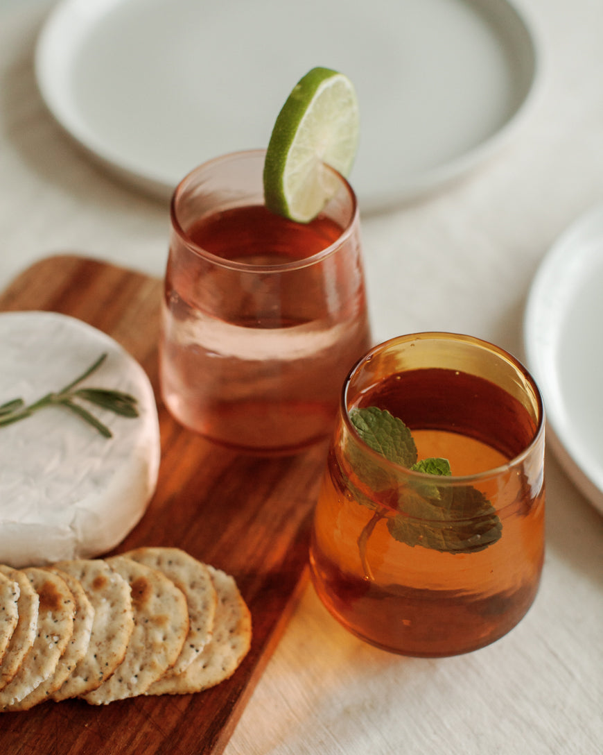 Two glasses of red drinks with garnishes on a wooden board with crackers.