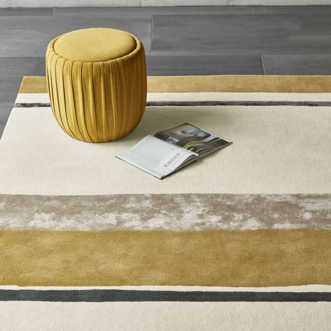 Yellow pouf on a striped rug with a magazine next to it