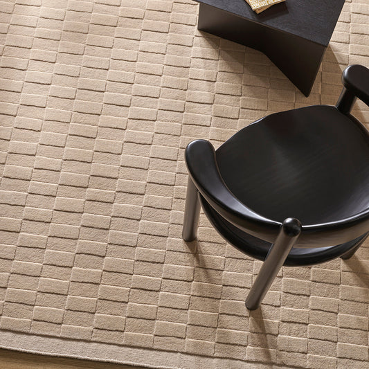 Beige textured rug with a black chair and table in a room setting