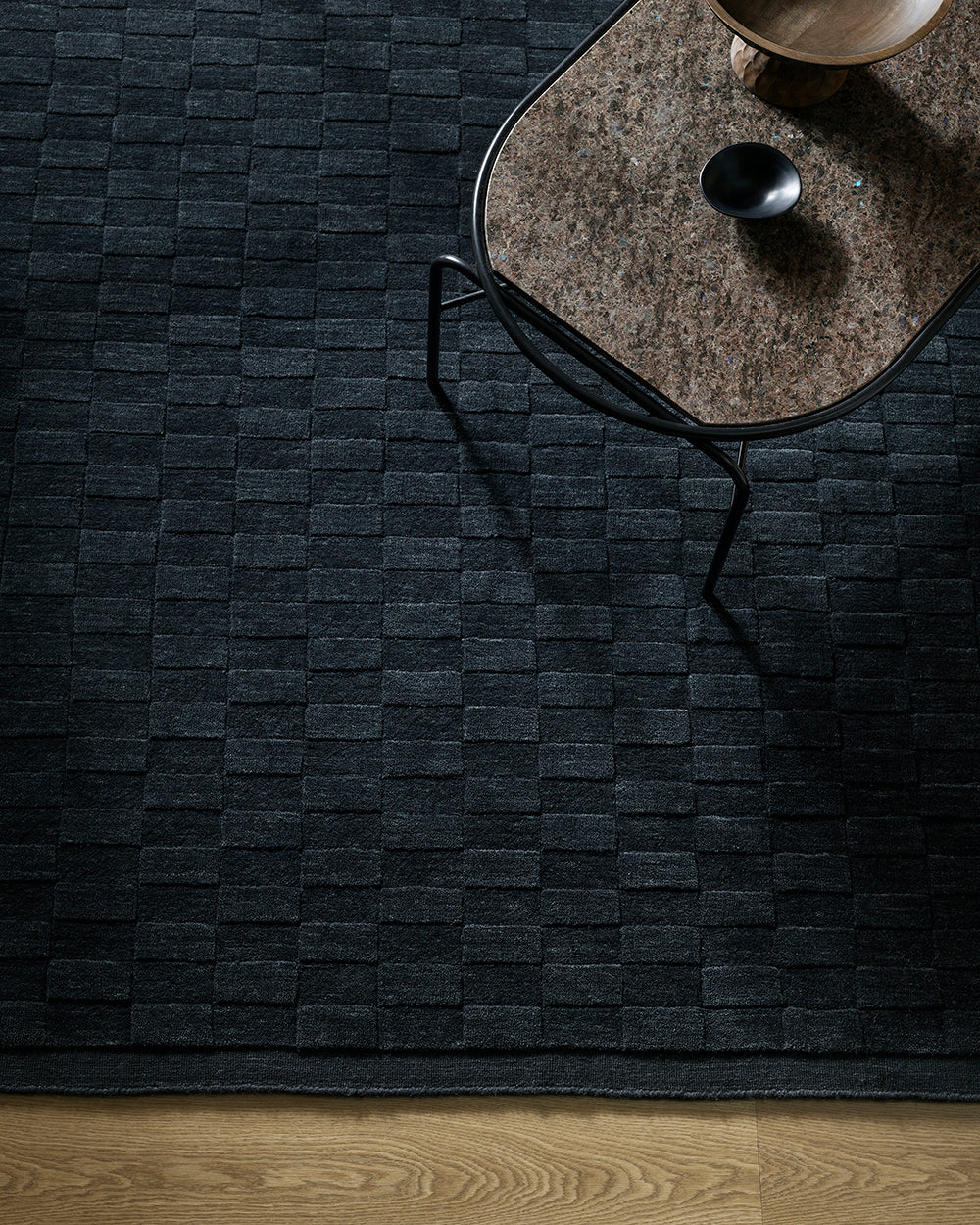 Dark woven rug with a marble table and candle on a wooden floor