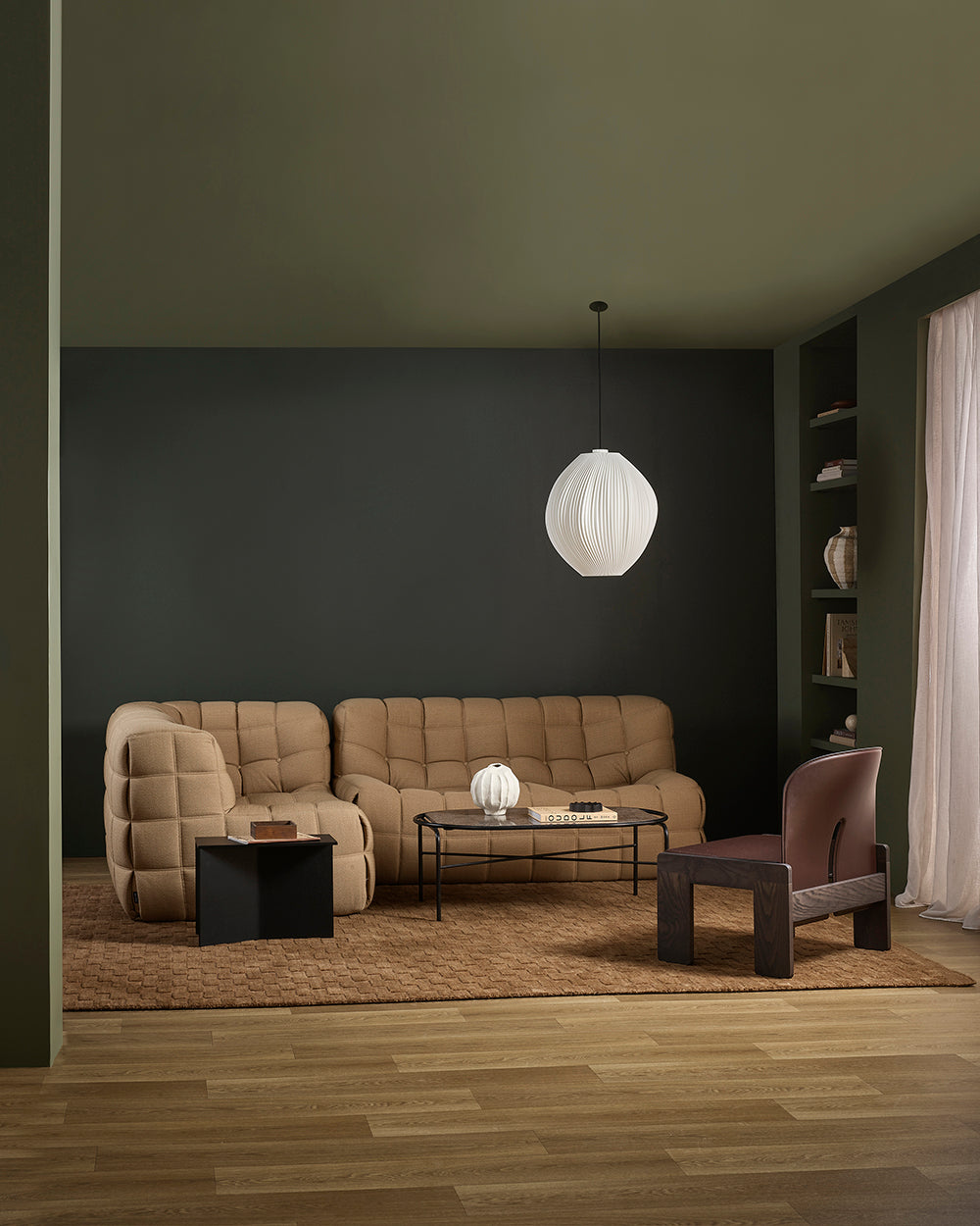 Modern living room with a beige sofa, armchair, and coffee table under a white pendant light.