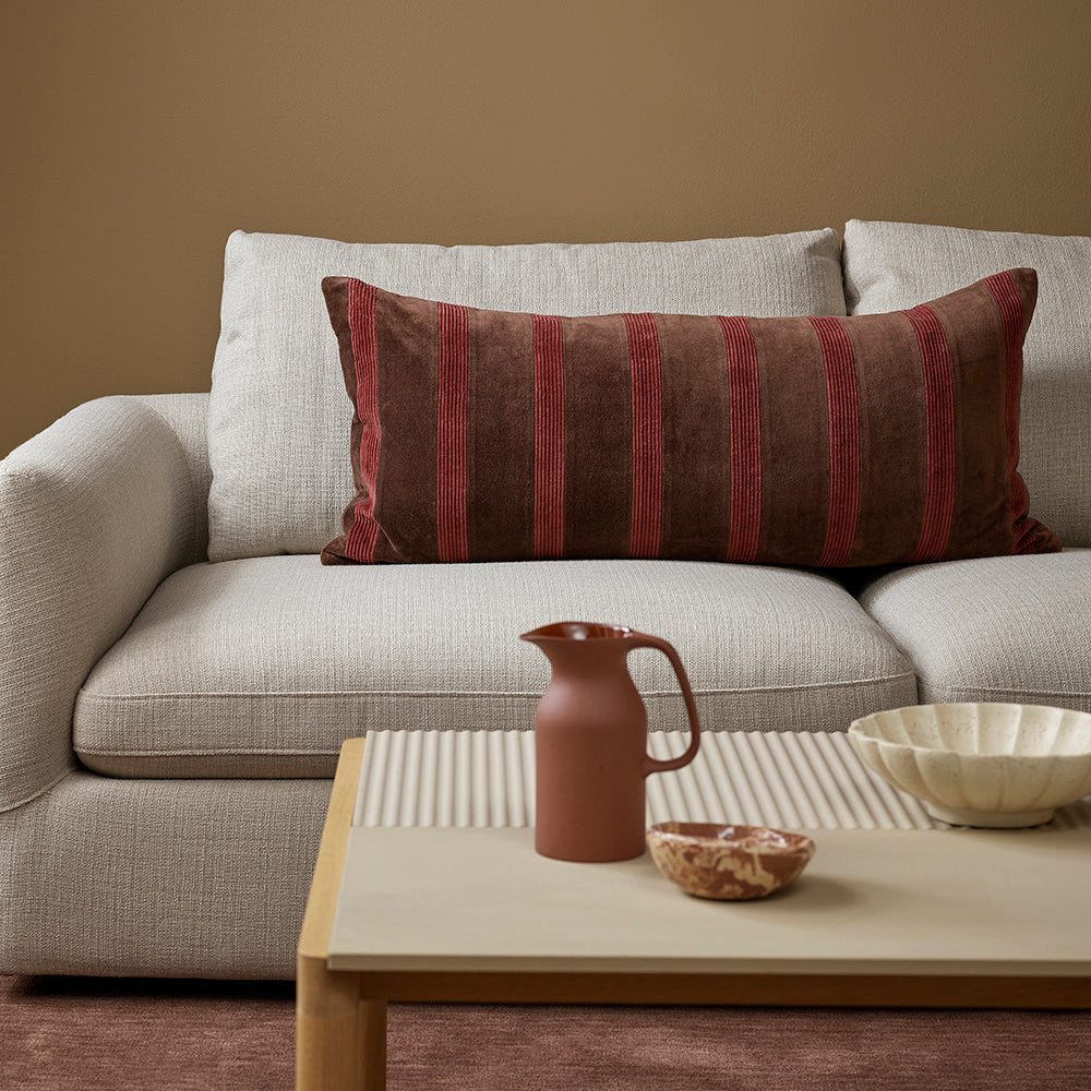 Gray sofa with a striped pillow, wooden coffee table with decorative items, and brown wall.