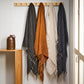 4 Indira linen throws in noir, tabacco, almond and french navy haniging from wood pegs against a white wall with a wood shelf and rustic cider bottle beside it