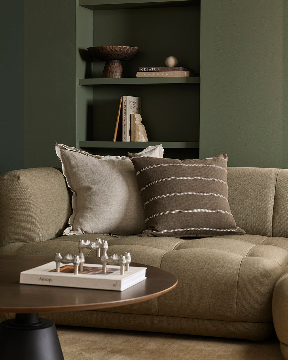 Green sofa with decorative pillows in a room with a bookshelf.