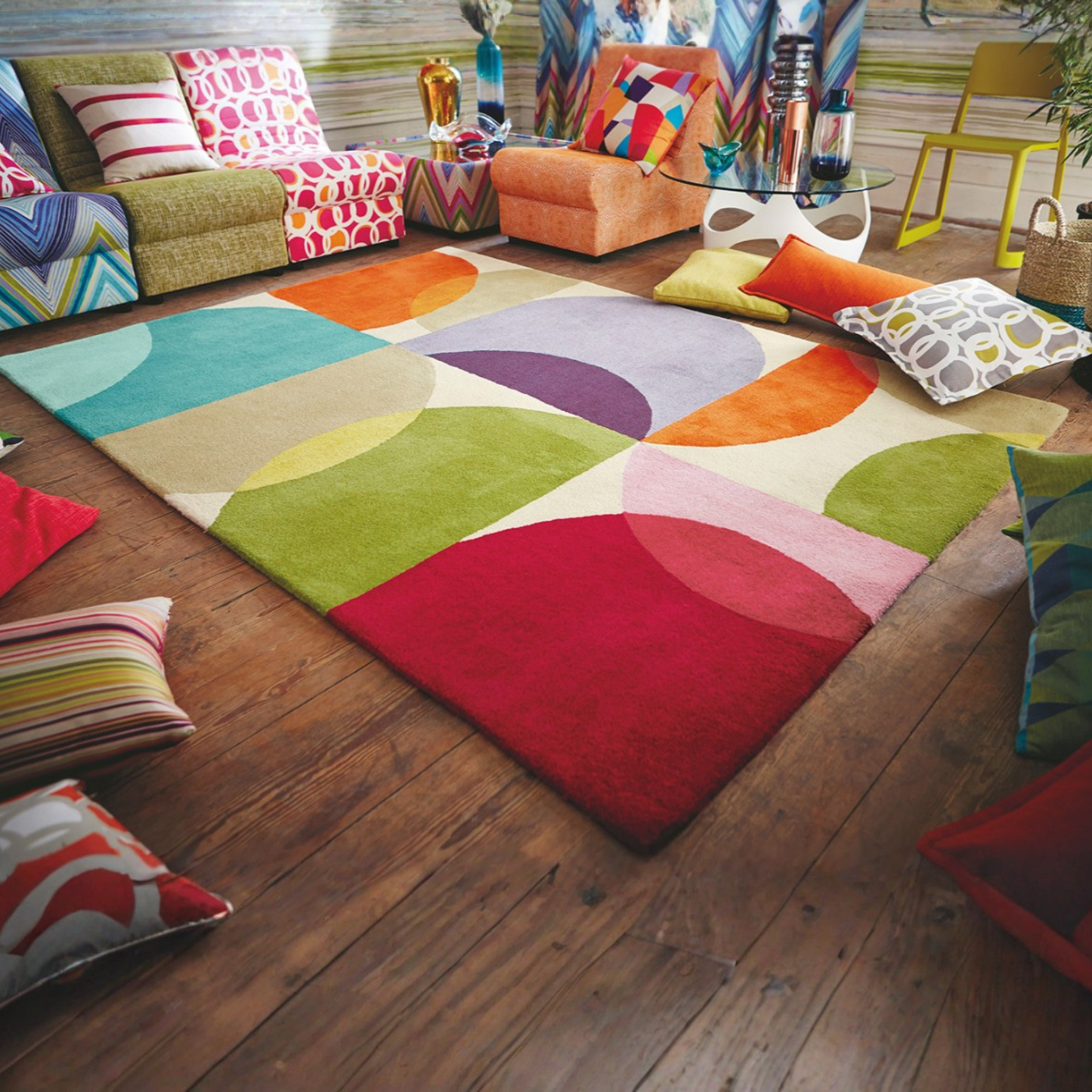 A colorful area rug with large overlapping semi-circles in red, pink, orange, yellow, green, purple, and beige, styled in a modern living room on a dark wood floor.