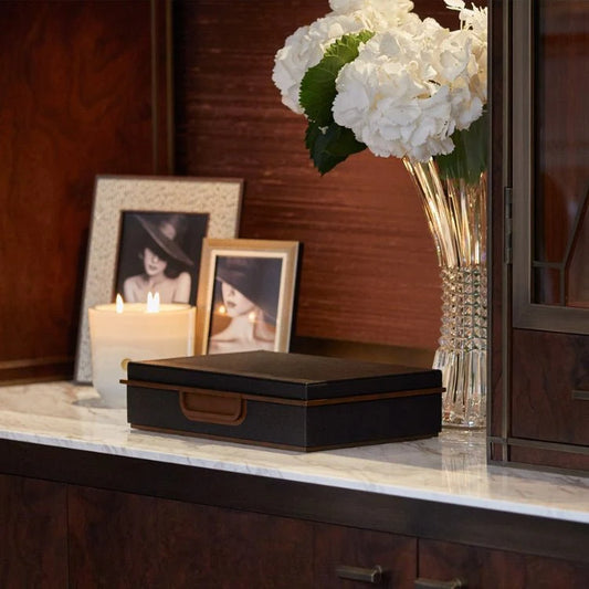 Decorative setting with a black box, white flowers in a vase, and framed photos on a wooden surface.