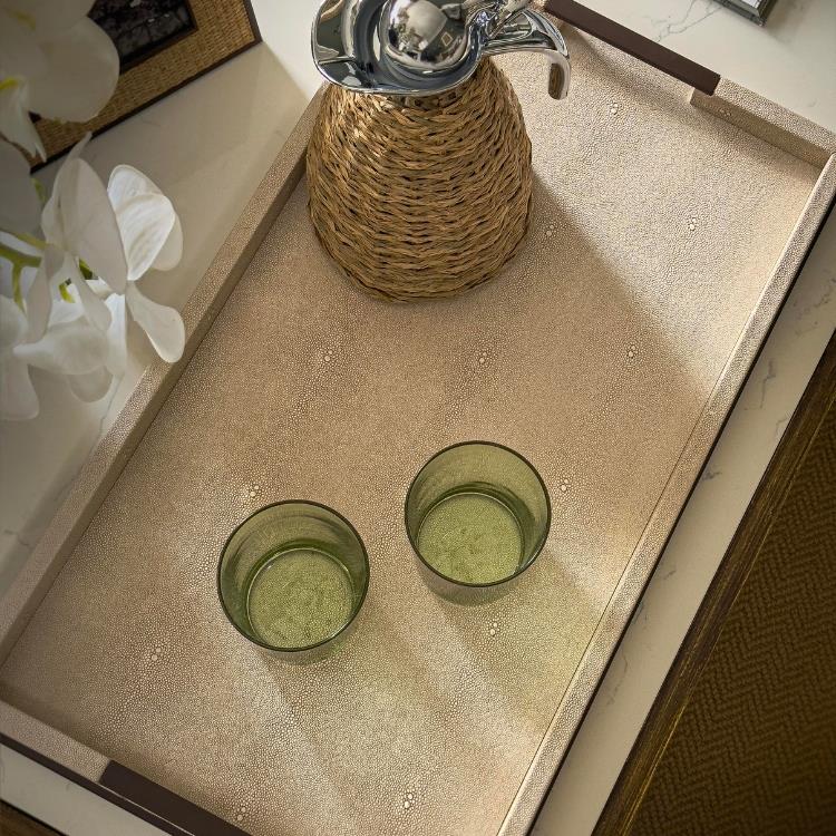 Two green glass tumblers on a textured surface with a woven container and white flowers in the background.