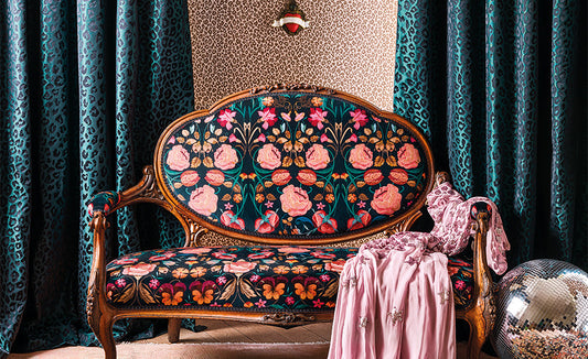 Bonita Velvet Rosa floral fabric from Temperley London and Roma Fabrics in pinks, aqua, orange and green on a black background covering a french style historic sofa with green jaguar print curtains