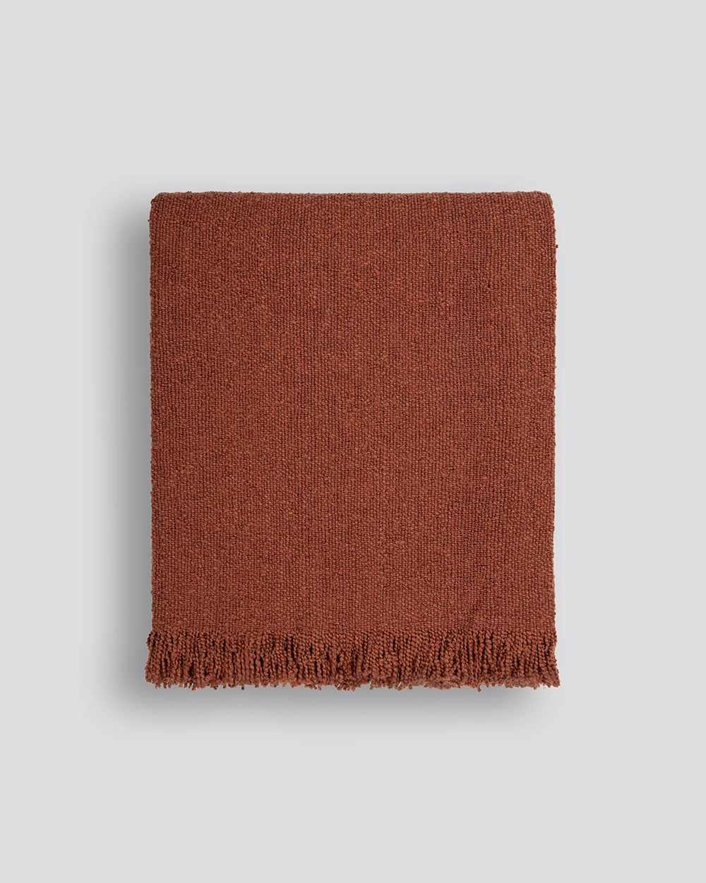 Brown woven blanket with frayed edges on a light gray background