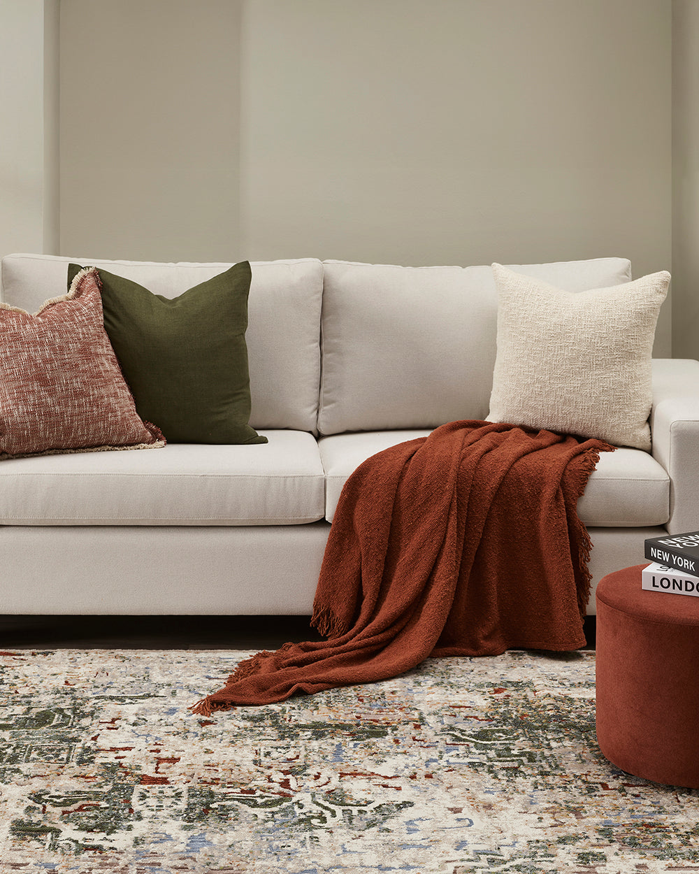 White sofa with decorative pillows and a blanket on a patterned rug in a living room setting.