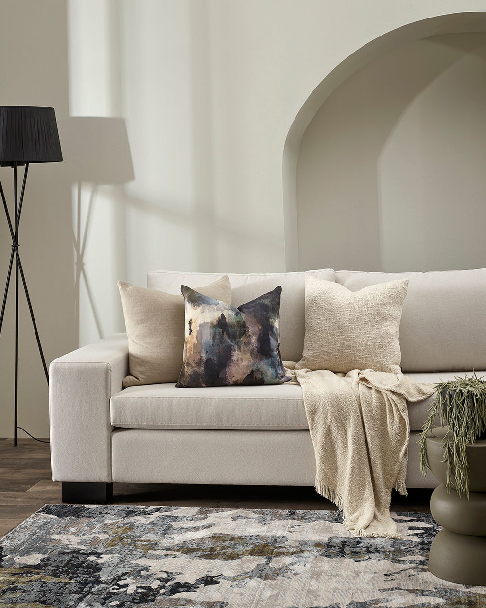 Beige sofa with decorative pillows and a blanket in a living room setting.