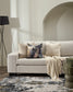 Beige sofa with decorative pillows and a blanket in a living room setting.