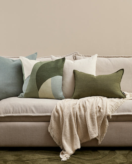Gray sofa with decorative pillows and a blanket on a neutral background