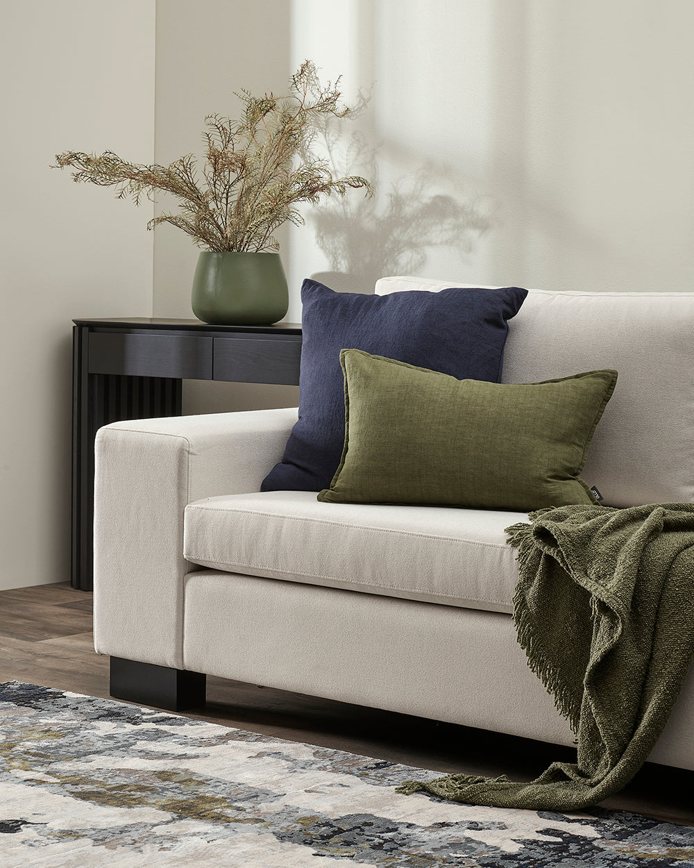 White sofa with green and blue pillows and a plant in a room.