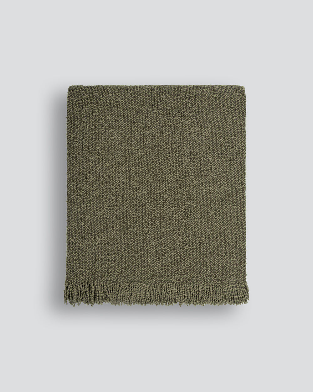 Green woven blanket with fringes on a light gray background