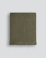 Green woven blanket with fringes on a light gray background