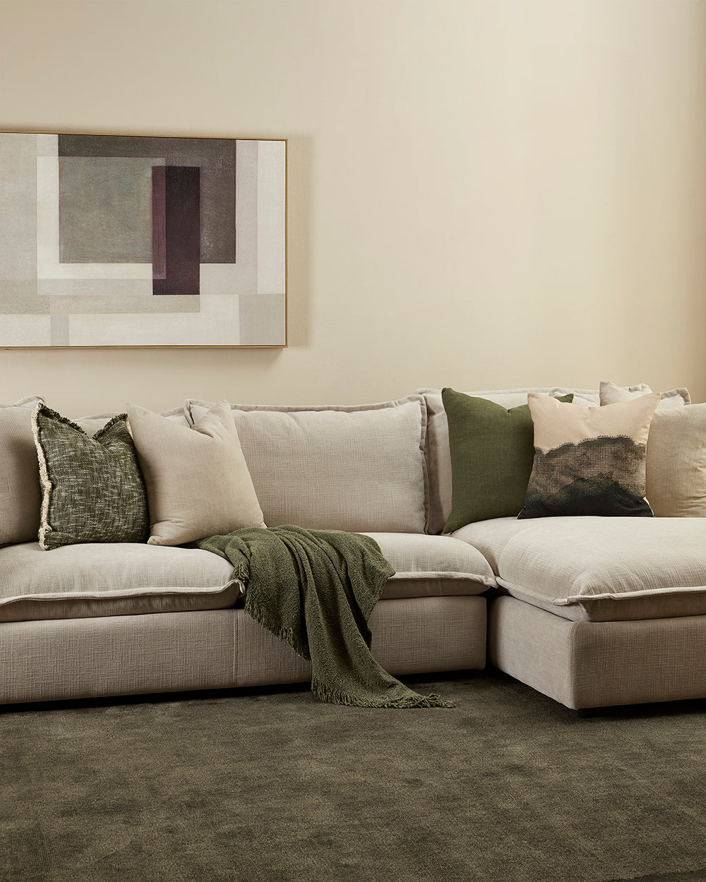 Beige sectional sofa with decorative pillows and a green blanket in a living room setting.