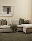 Beige sectional sofa with decorative pillows and a green blanket in a living room setting.