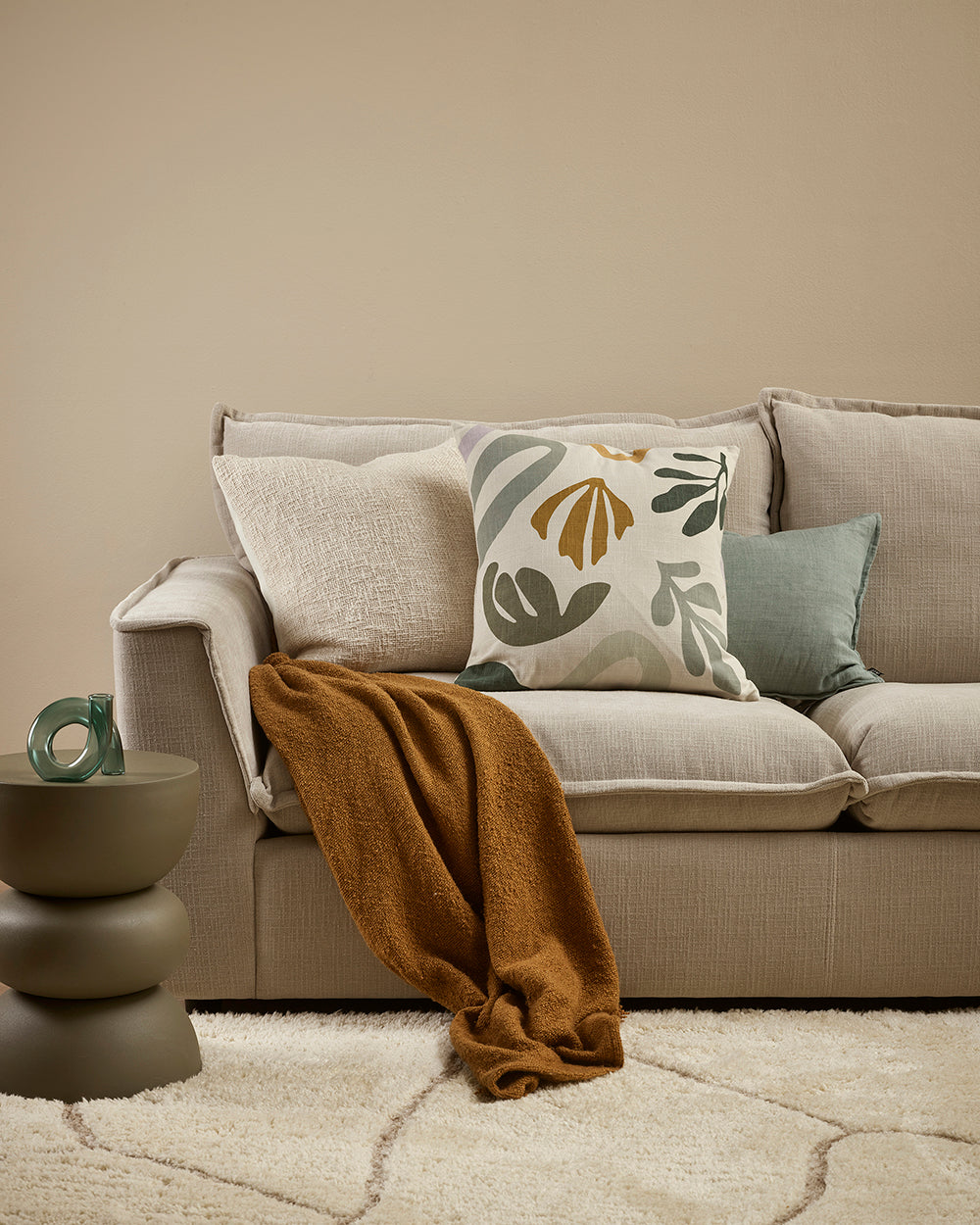 Beige sofa with decorative pillows and a blanket in a living room setting.